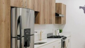 A modern kitchen with wooden cabinets, stainless steel appliances, and a white countertop. - House Valencia 1 (Flores)