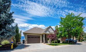 A residential house with a garage, driveway, and a tree in the front yard. - The home base for your Kelowna experience! (Kelowna)