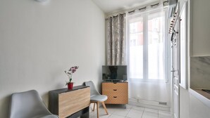 A modern living room with a TV, two chairs, a small wooden cabinet, and a potted orchid. - Magnificent studio just outside Paris (Clichy)