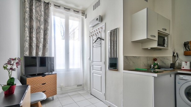 A compact living space with a TV, a small dining area, a kitchen with a washing machine, and a door with a coat rack. - Magnificent studio just outside Paris (Clichy)
