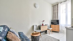 A modern living room with a sofa, a coffee table, a TV, and a small dining area. - Magnificent studio just outside Paris (Clichy)