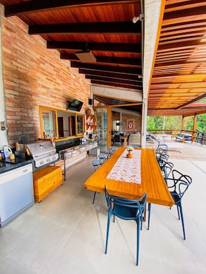 An outdoor kitchen with a grill, dining table, and chairs. - Paraiso em Juquehy (São Sebastião)