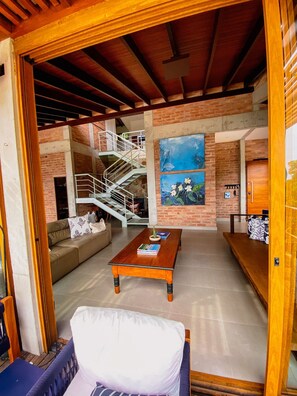 Un amplio salón con una escalera, una mesa de centro con libros, un sofá y un cuadro en la pared.