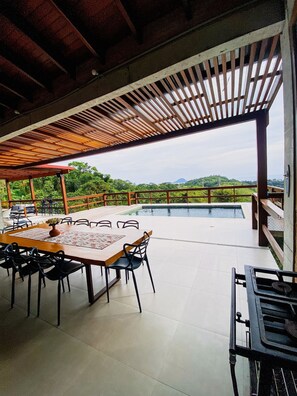 An outdoor dining area with a pool, wooden pergola, and a view of the landscape. - Paraiso em Juquehy (São Sebastião)