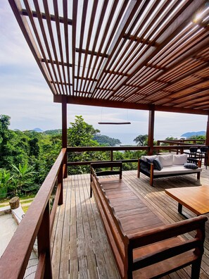 A wooden deck with a bench and a table, overlooking a lush landscape and a body of water. - Paraiso em Juquehy (São Sebastião)