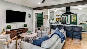 Una sala de estar moderna con sofá, mesa de centro y televisión. Cuenta con una cocina con nevera y una mesa de comedor.