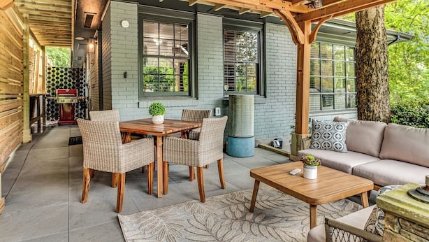 Une terrasse couverte avec une table et des chaises en bois, un canapé et un barbecue.