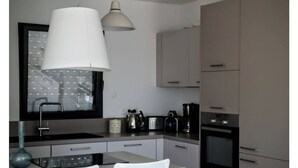 Een moderne keuken met een groot raam, een witte hanglamp en inbouwapparatuur.