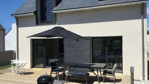 Een modern huis met een patio, inclusief een barbecue, buitenmeubilair en een grote parasol.