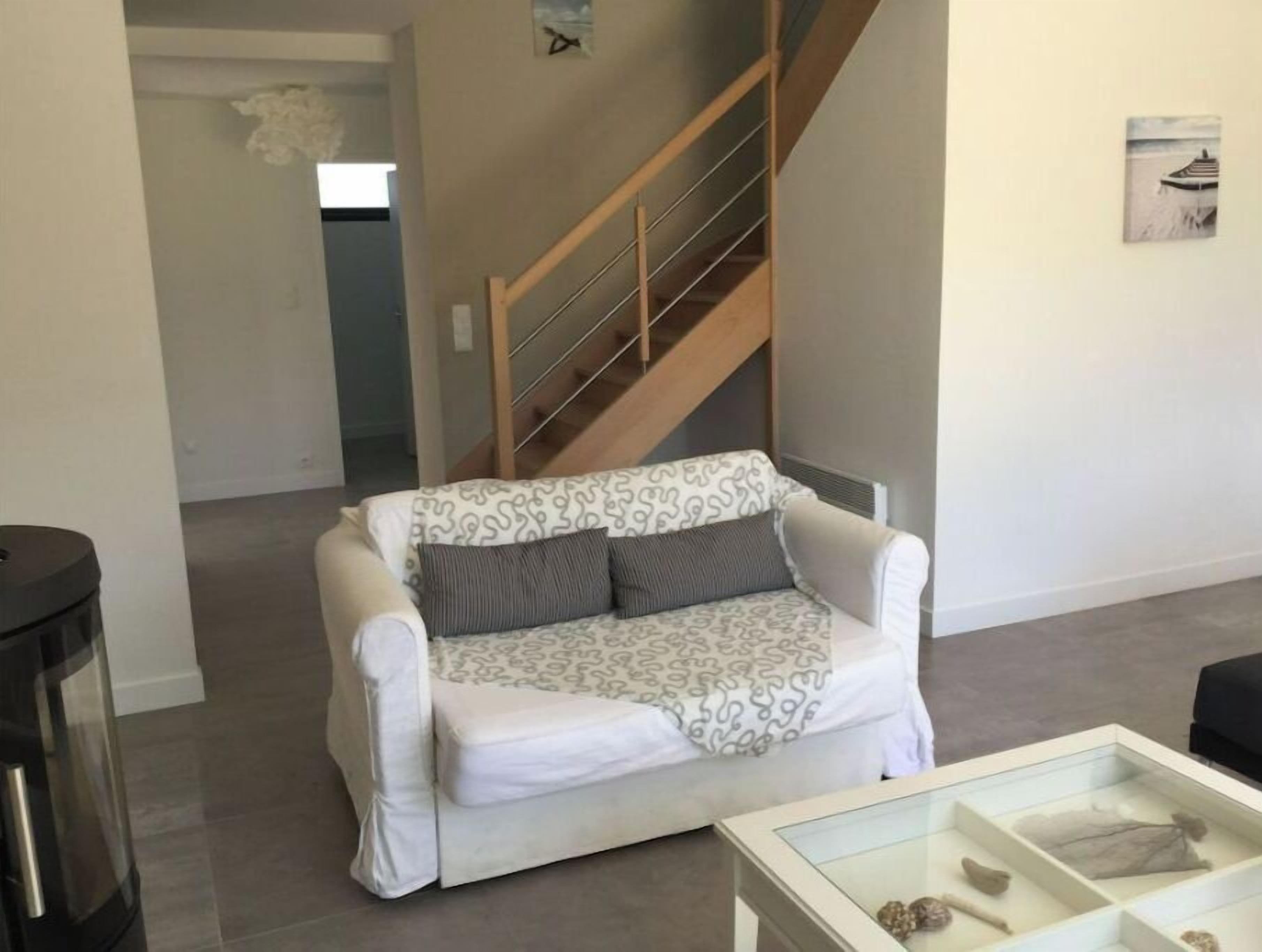 Una sala de estar con un sofá blanco, una mesa de centro de cristal y una escalera de madera.