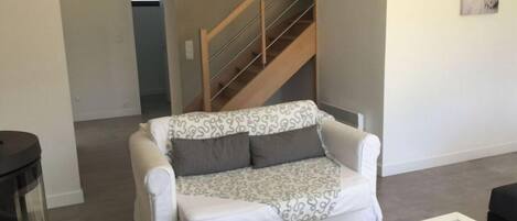 Una sala de estar con un sofá blanco, una mesa de centro de cristal y una escalera de madera.