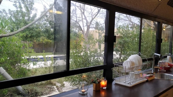 Enjoy a garden view from the large window, with a kitchen area featuring a sink, dish rack, and candle.
