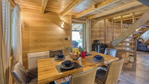 Ein Holzinterieur mit einem für vier Personen gedeckten Esstisch, umgeben von Ledersesseln. Auf dem Tisch steht eine Obstschale und eine rote Tasse.