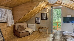 Ein gemütliches Schlafzimmer im Dachgeschoss mit Holzbalken, einer Couch, einem Bett, einem Heizkörper und Blick ins Grüne.