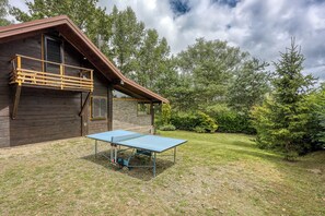 En stuga av trä med en balkong, ett bord för bordtennis och en gräsyta med träd.