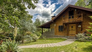 Eine Holzdiele mit Balkon, umgeben von einem gepflegten Garten und einem gepflasterten Weg.