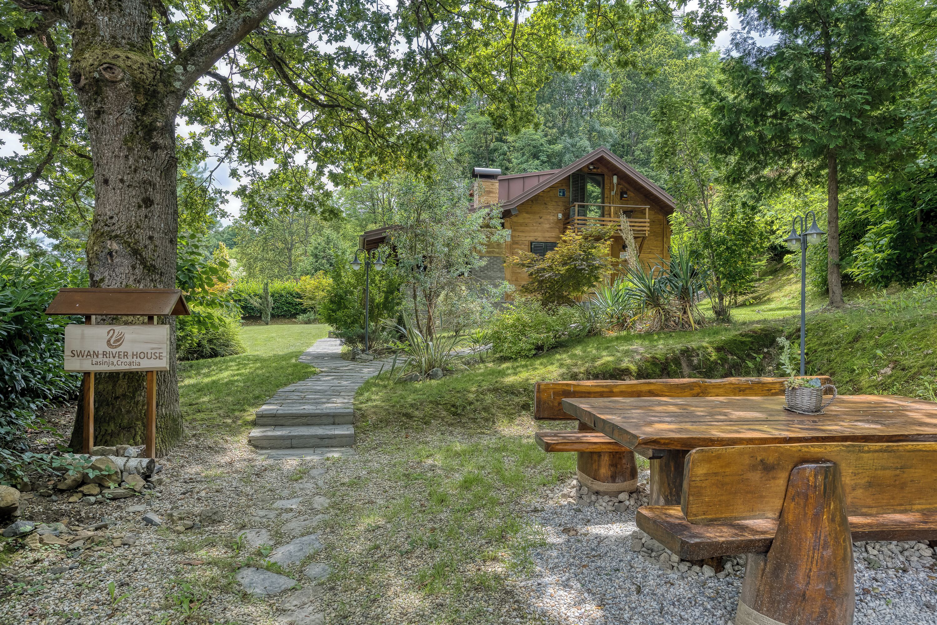 A wooden cabin with a stone pathway leading to it, surrounded by lush greenery and a picnic table.