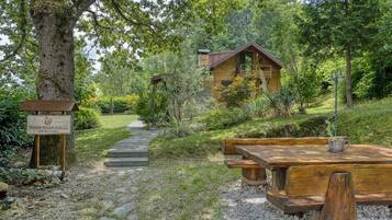 A wooden cabin with a stone pathway leading to it, surrounded by lush greenery and a picnic table.