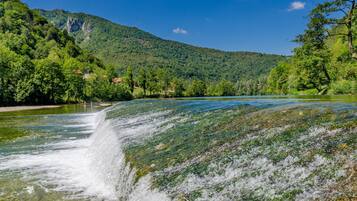 A waterfall cascading into a river surrounded by lush greenery and mountains.