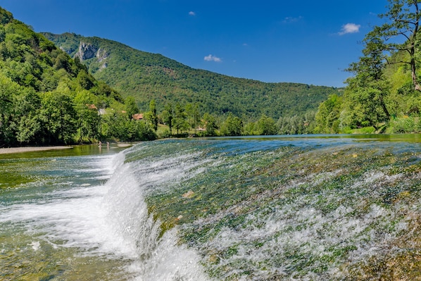 A waterfall cascading into a river surrounded by lush greenery and mountains. - Swan River House With Sauna & Jacuzzi (Lasinja)
