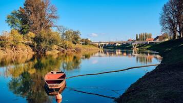 A calm river with a small boat docked on the left, a bridge in the background, and trees lining the riverbank.