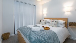 Una cama bien hecha con ropa de cama estampada, una mesita de noche con una cesta y lámparas fijadas a la pared.