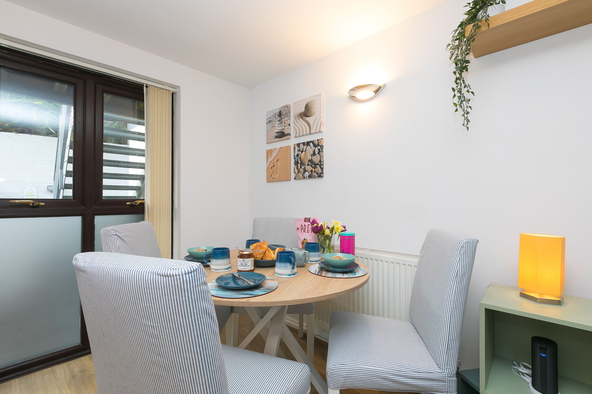 A dining area with a round table, striped chairs, and a wall-mounted light fixture.