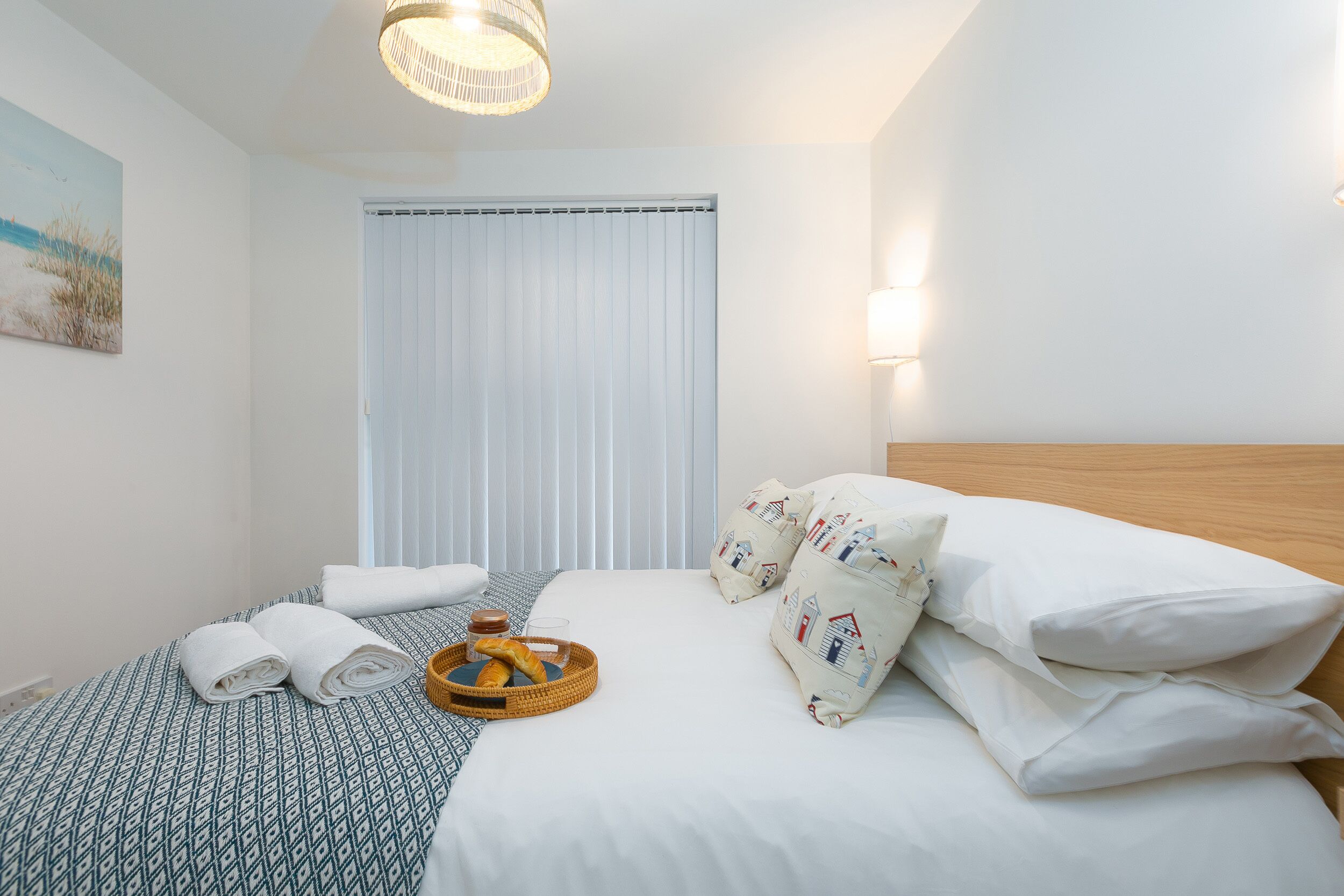 A neatly made bed with white linens, a basket of bread, and a tray with a drink.
