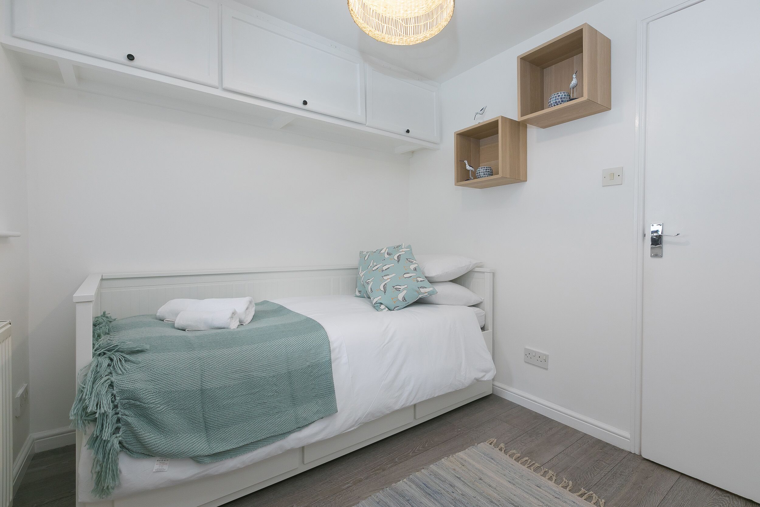 A neatly arranged bedroom with a bed, a bedside table, a wardrobe, and a shelf with decorative items.