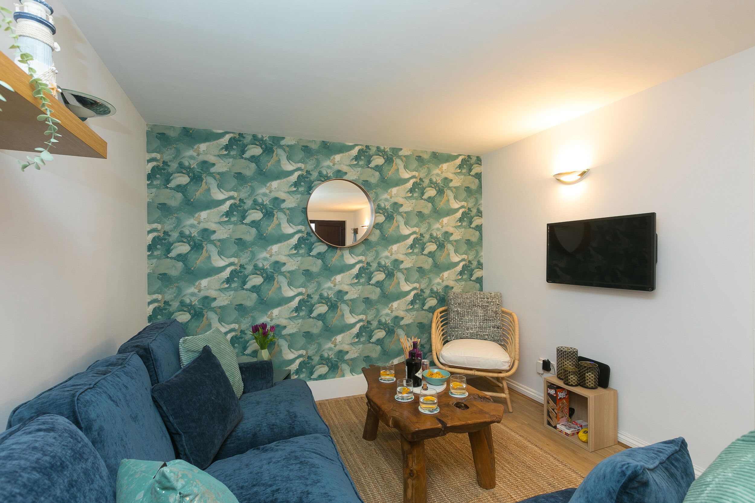 A cozy living room with a blue sofa, a round mirror, and a wooden coffee table with snacks.