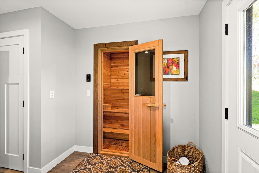 A wooden sauna room with a glass door, a patterned rug, and a wicker basket.