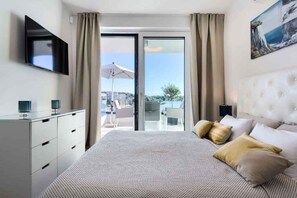 A modern hotel room with a large bed, a flat-screen TV, a sliding glass door to a balcony, and a view of the sea. - Villa with pool and sea view (Pješćana Uvala)