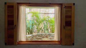 Una ventana con contraventanas de madera, un alféizar de piedra y plantas tropicales afuera.