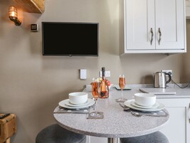 A modern kitchen with a round granite table, white cabinets, a flat-screen TV, and a kettle.