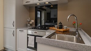 Uma cozinha moderna com armários brancos, uma pia de aço inoxidável, um fogão a gás e uma cafeteira sobre a bancada.