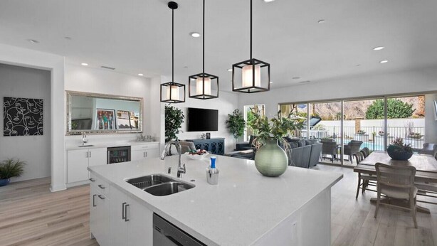 Une cuisine moderne dotée d’un îlot central, de luminaires suspendus et d’un coin repas offrant une vue sur l’extérieur.