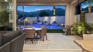 Une terrasse extérieure moderne, dotée d'une piscine, de meubles en osier et d'un téléviseur à écran plat.