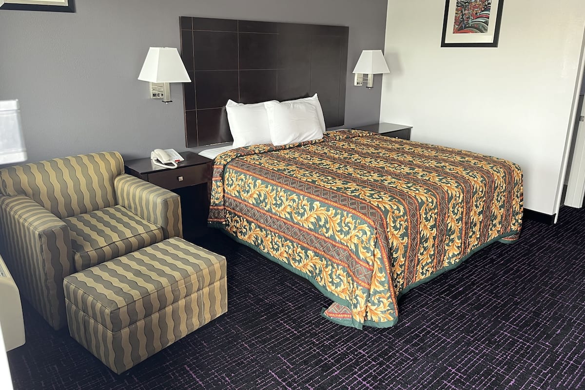 Une chambre d’hôtel comprenant un lit, deux tables de chevet, un téléphone, un canapé et un pouf.