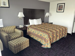 A hotel room with a bed, two nightstands, a telephone, a sofa, and an ottoman. - Broadway Inn (San Antonio)