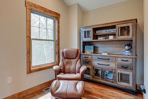 A room with a leather recliner chair, a wooden cabinet with drawers, and a large window.