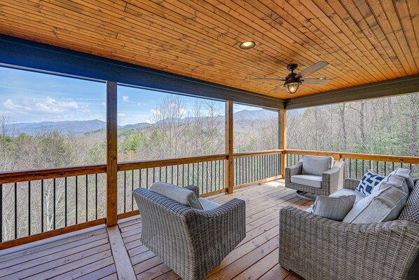 A covered outdoor deck with wicker furniture and a ceiling fan.