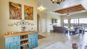 A spacious living room with a wooden ceiling, a blue cabinet with decorative items, a gray sofa, and a large window offering a view. - Unique Las Cruces Home w/ Patio + Gas Grill! (Las Cruces)