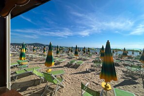 A beach with rows of green and yellow beach chairs and umbrellas, a clear sky, and a calm sea in the background.
