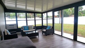Uma sala de sol com grandes janelas, um sofá, uma poltrona e uma mesa de centro.
