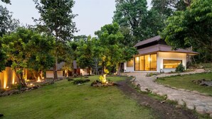 A modern house with a stone pathway leading to a glass door entrance, surrounded by lush greenery and a well-maintained lawn. - Zen Maekampong Waterfall Ryokan (.)