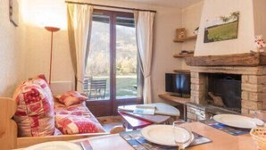 Una sala de estar acogedora con chimenea, una zona de comedor con mesa para dos personas, y un gran ventanal con cortinas.