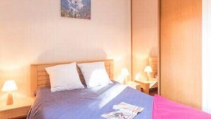 Habitación de hotel con cama, mesita de noche con lámpara, un cuadro en la pared y un armario de madera.