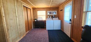 A narrow hallway with wooden walls and a carpeted floor. There are two white washing machines and a small table with a plant.