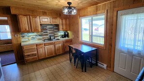 A wooden kitchen with a stone backsplash, a dining table with chairs, and a door with a window. - River Bend Cottage (White Cloud)