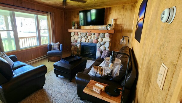 A cozy living room with a fireplace, leather sofas, a coffee table, and a TV mounted on the wall. - River Bend Cottage (White Cloud)